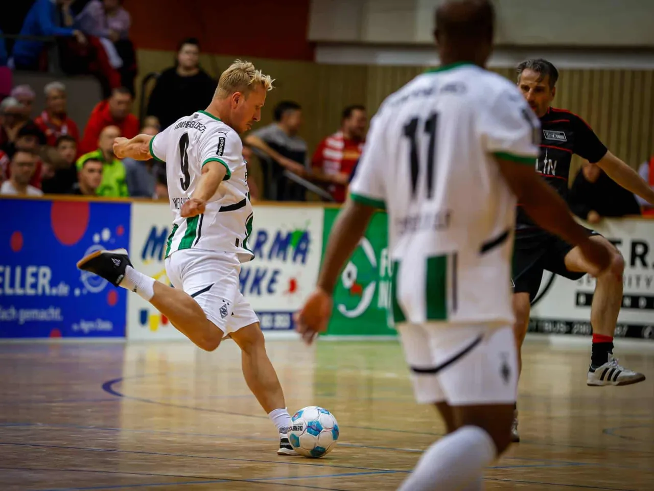 Spieler in weißen Trikots am Ball vor den Zuschauerrängen.